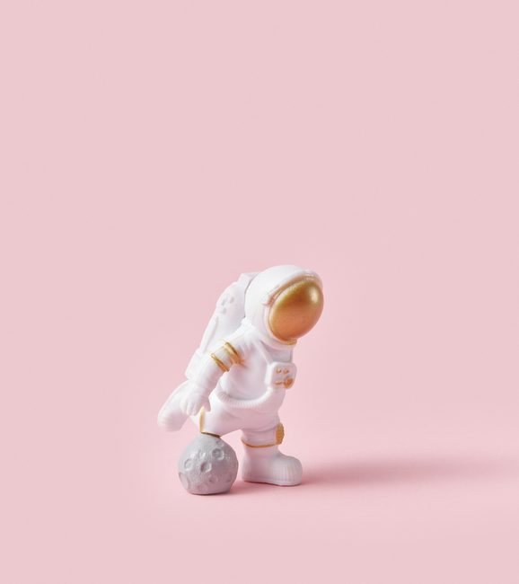 Cosmonaut in space suit using moon ball for playing football over pink studio background. Sport activity of astronaut. Isolated.