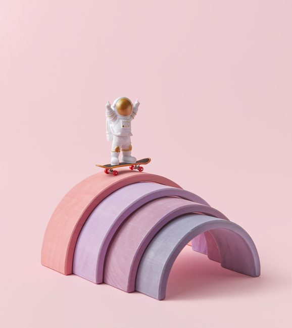 Satisfied astronaut in spacesuit standing on top of springboard with skateboard. Time spending with extreme. Pink studio background.